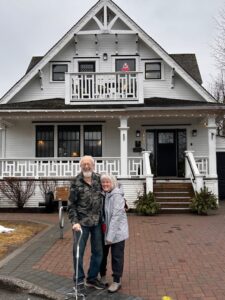 White house with elderly man and younger woman standing in front of it. 
