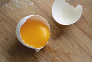 A white egg cracked open with the yellow yolk exposed on one side and the other half of the shell is empty. 
